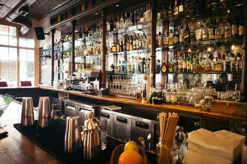 An empty, warmly lit bar with amber bottle shelves, candles and wooden stools.