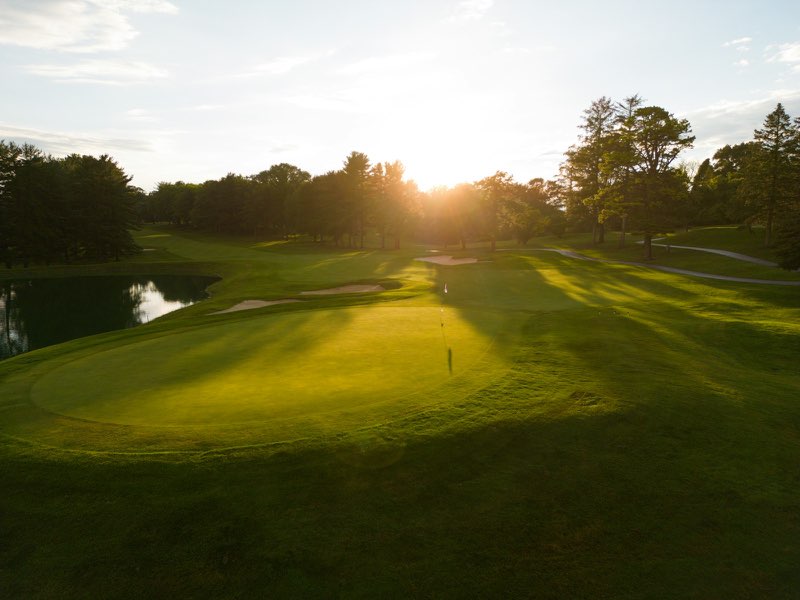 Low sun glowing over a golf green, pond and tree line.