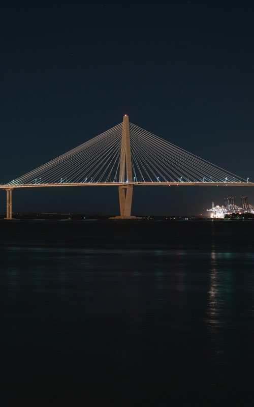 A cable-stayed bridge lit at night over dark water.